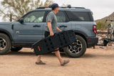 Person carrying a large black box next to a vehicle with bicycles on a bike rack in a desert setting.